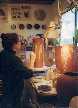 Jeannine decorating a vase at her studio workbench
